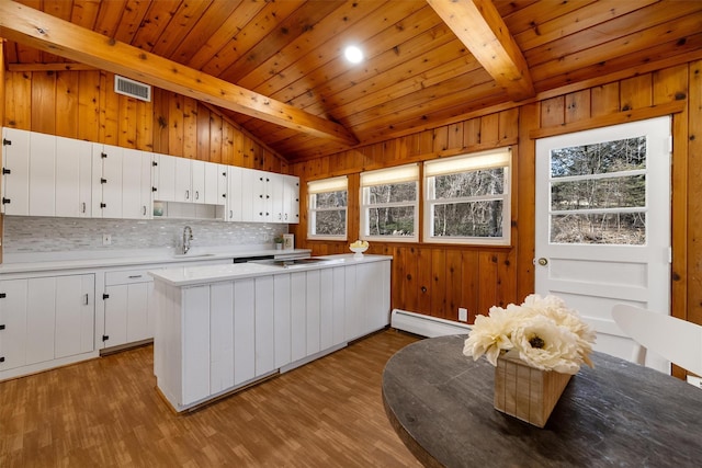 kitchen with a sink, lofted ceiling with beams, white cabinetry, and a baseboard radiator