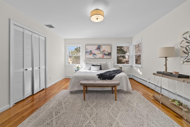 bedroom featuring visible vents, a baseboard heating unit, baseboards, wood finished floors, and a closet