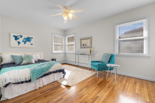 bedroom with baseboards, wood-type flooring, a baseboard heating unit, and a ceiling fan