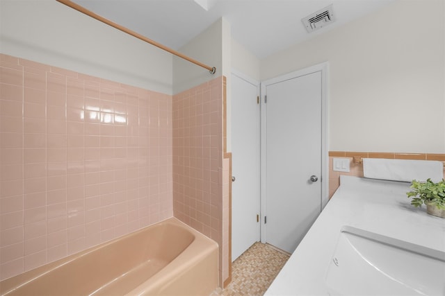 bathroom featuring visible vents, shower / bathtub combination, tile patterned floors, tile walls, and a sink