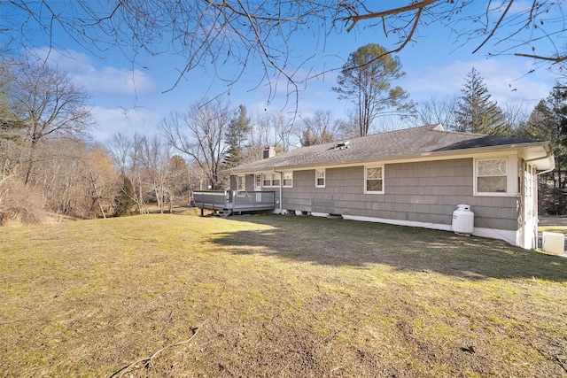 back of property with a chimney, a wooden deck, and a yard