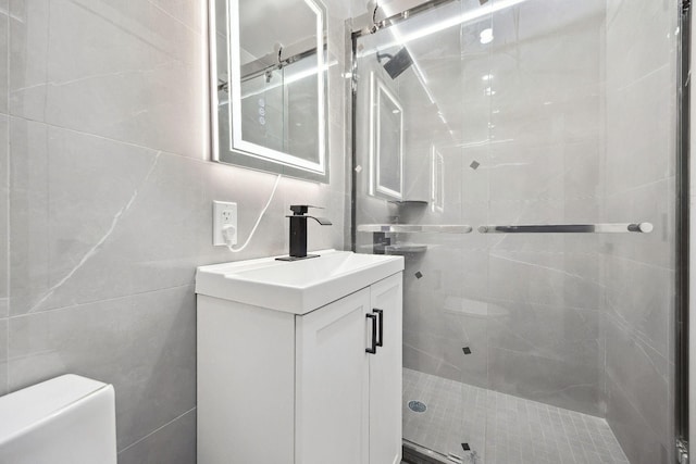 bathroom with vanity, tiled shower, tile walls, and toilet