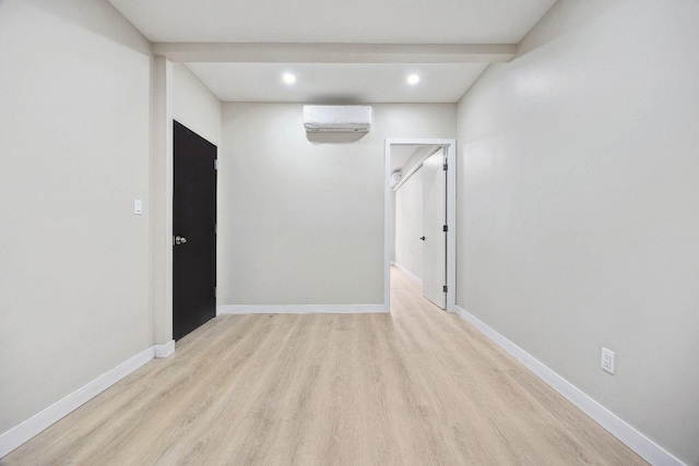 spare room featuring beamed ceiling, light hardwood / wood-style floors, and a wall mounted AC