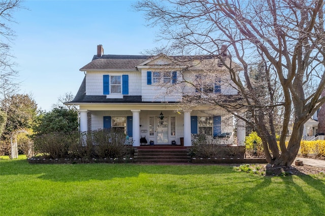 traditional-style house with covered porch, roof with shingles, a chimney, and a front yard