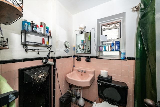 bathroom with toilet, a wainscoted wall, tile walls, and a sink