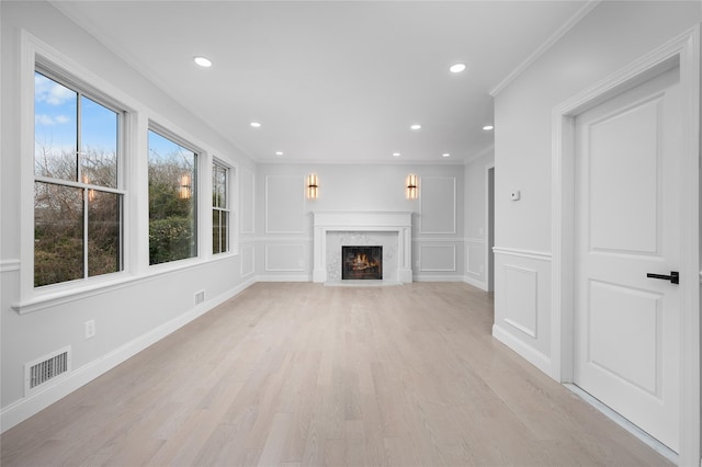 unfurnished living room with crown molding, visible vents, a decorative wall, and light wood-style flooring