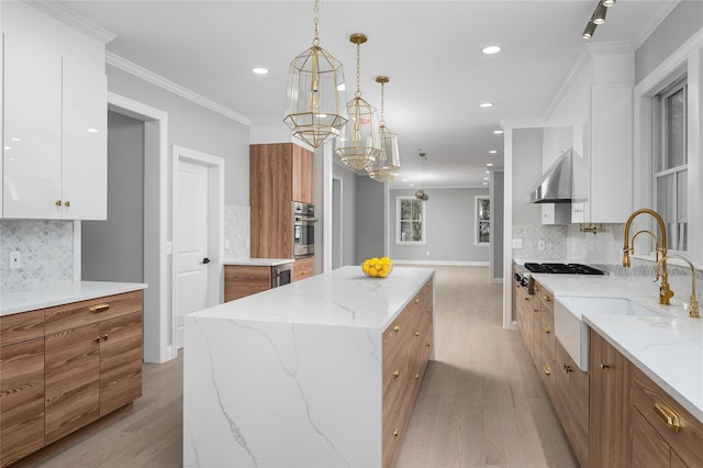 kitchen with brown cabinets, stainless steel oven, a sink, and wall chimney exhaust hood