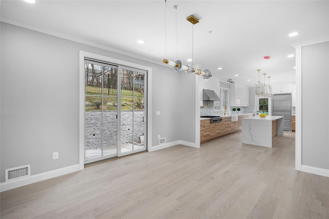 interior space featuring stainless steel appliances, a kitchen island, visible vents, wall chimney exhaust hood, and light wood finished floors