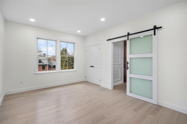 unfurnished room with a barn door, recessed lighting, light wood-style flooring, and baseboards