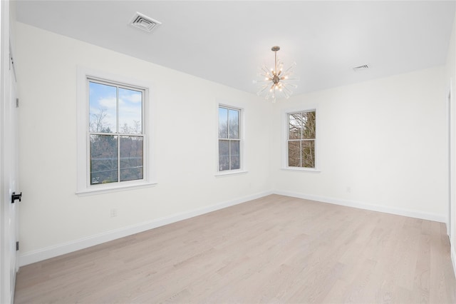 spare room with light wood finished floors, baseboards, and a notable chandelier