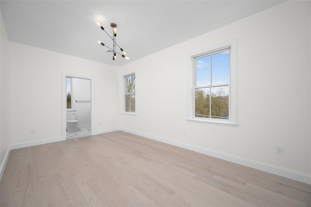 spare room with light wood-type flooring, an inviting chandelier, and baseboards