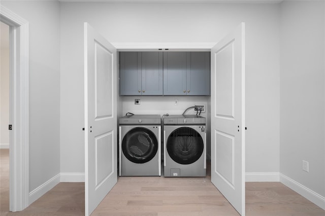 clothes washing area with cabinet space, light wood-style flooring, baseboards, and washing machine and clothes dryer