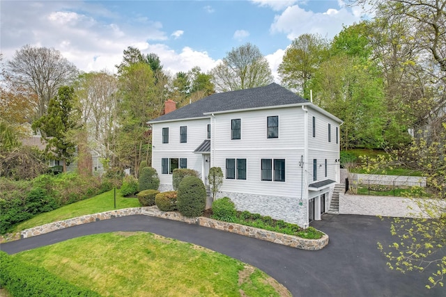 colonial inspired home featuring an attached garage, driveway, stone siding, a chimney, and a front yard