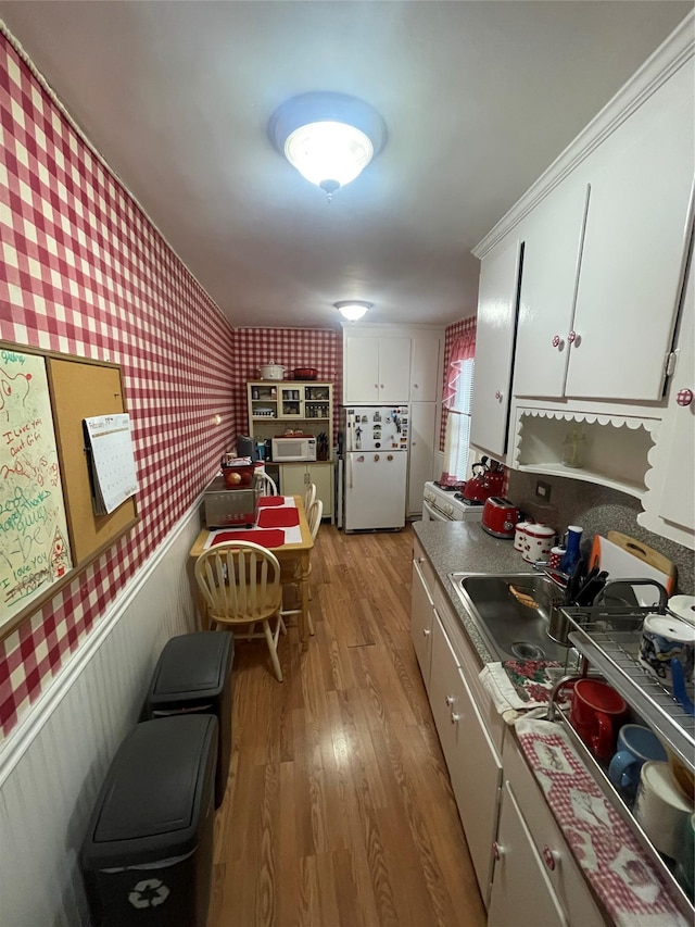 kitchen with white cabinetry, a sink, light wood-type flooring, white appliances, and wallpapered walls