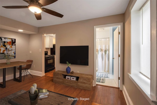 living area featuring a wealth of natural light, baseboards, wood finished floors, and a ceiling fan