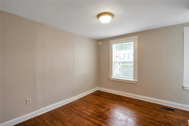 empty room featuring visible vents, baseboards, and dark wood-style floors