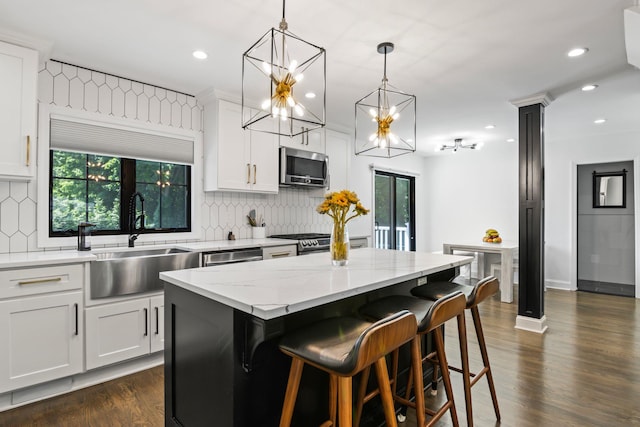 kitchen featuring stainless steel appliances, dark wood-style flooring, a sink, a center island, and decorative light fixtures