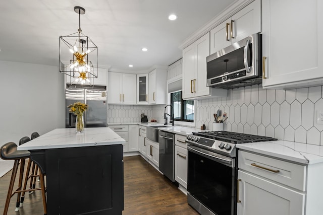 kitchen featuring dark wood-type flooring, a kitchen island, a sink, appliances with stainless steel finishes, and tasteful backsplash