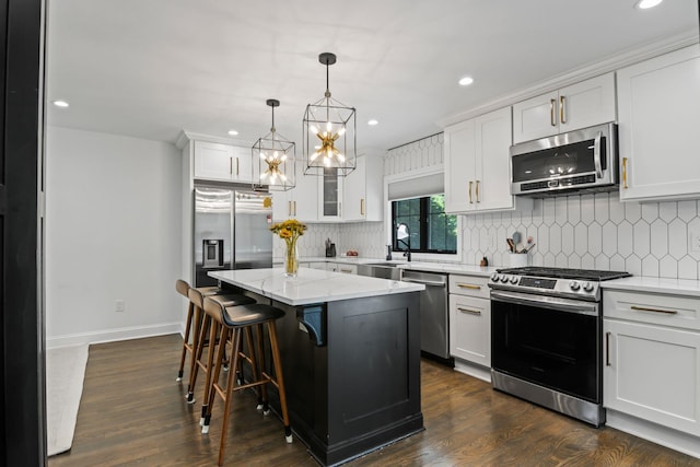 kitchen with dark wood finished floors, backsplash, appliances with stainless steel finishes, white cabinetry, and a kitchen island