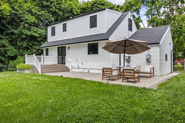 back of property with a deck, a patio, a lawn, and roof with shingles