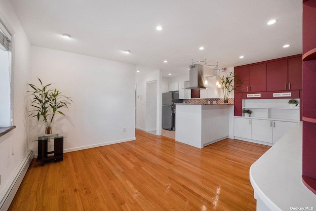 kitchen with stainless steel fridge, baseboard heating, white cabinetry, island range hood, and light hardwood / wood-style floors