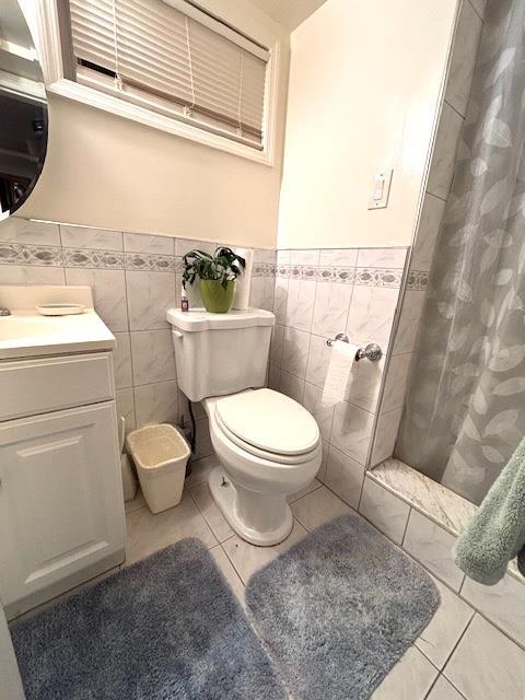 bathroom with toilet, a shower with curtain, tile walls, vanity, and tile patterned flooring