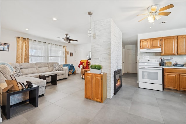 kitchen with a stone fireplace, under cabinet range hood, electric range, light countertops, and brown cabinets