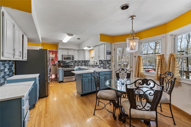 kitchen with white cabinetry, stainless steel appliances, blue cabinetry, and light hardwood / wood-style flooring