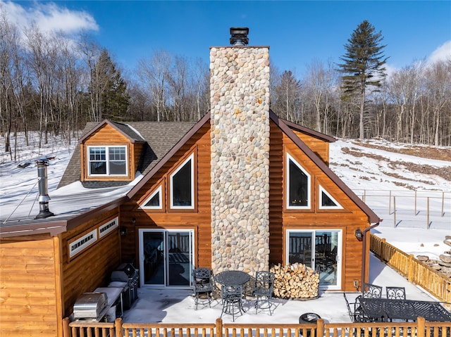 snow covered rear of property with a patio, a chimney, a shingled roof, outdoor dining space, and fence