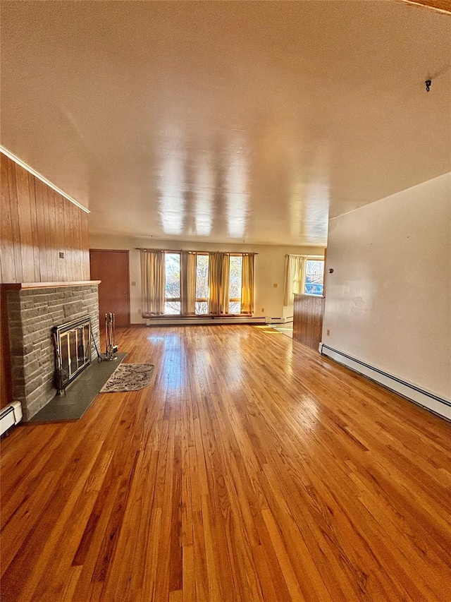 unfurnished living room with a baseboard heating unit, a fireplace, plenty of natural light, and wood finished floors