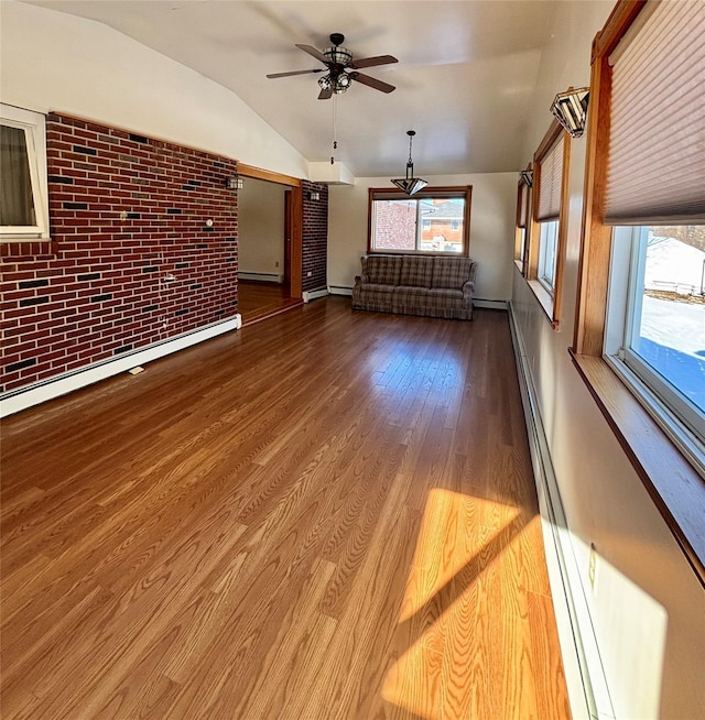 unfurnished living room featuring a wealth of natural light, brick wall, vaulted ceiling, and wood finished floors