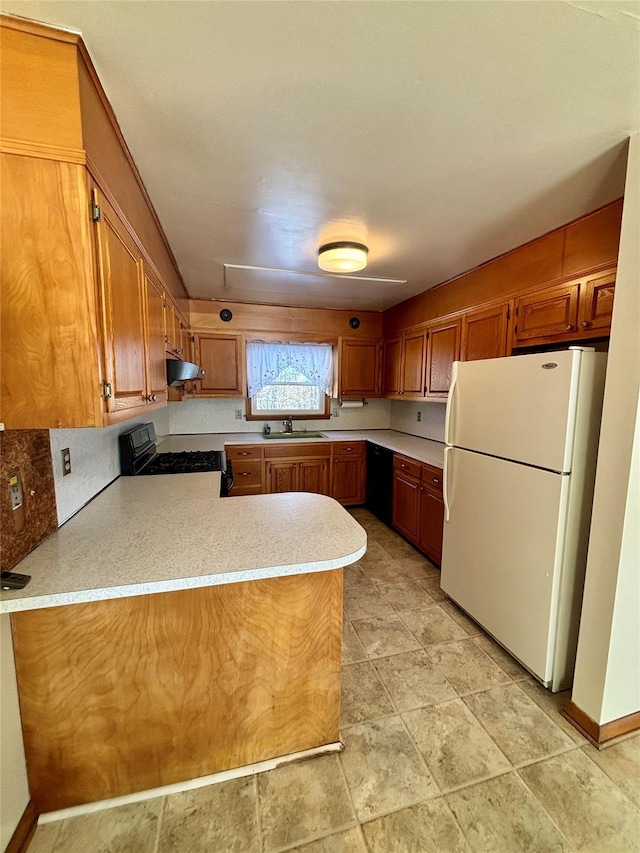 kitchen featuring brown cabinetry, freestanding refrigerator, a peninsula, black range with gas stovetop, and light countertops