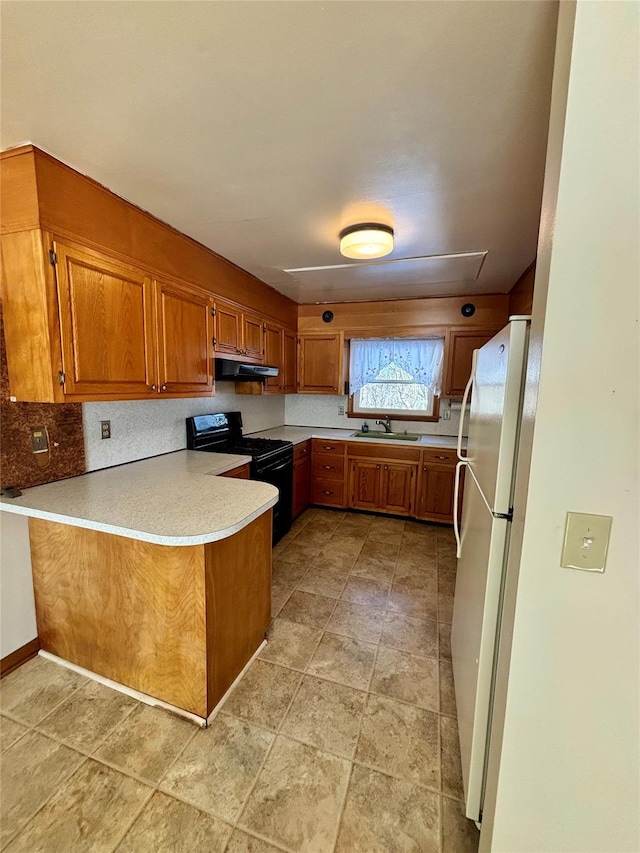 kitchen with under cabinet range hood, a peninsula, light countertops, freestanding refrigerator, and black range