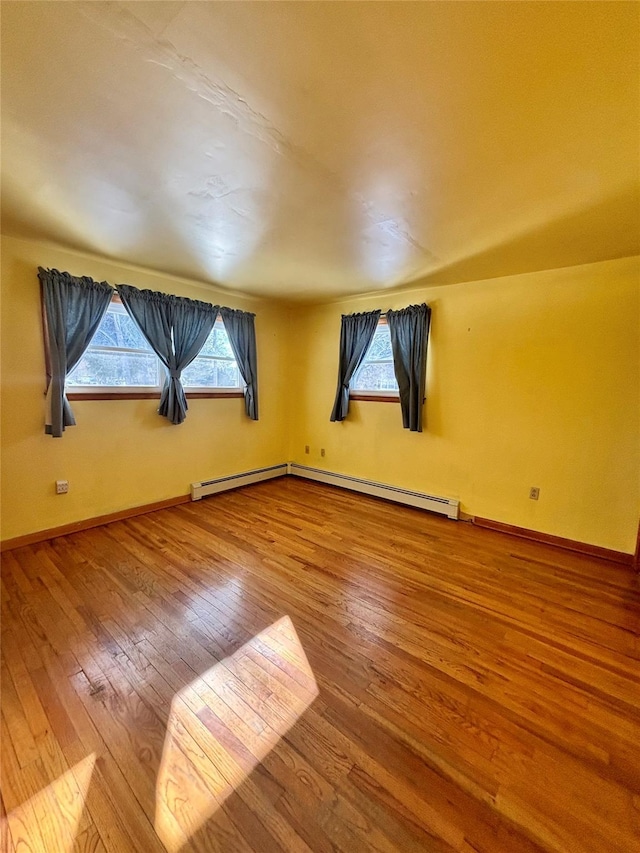 spare room with a baseboard radiator, a healthy amount of sunlight, baseboards, and wood finished floors