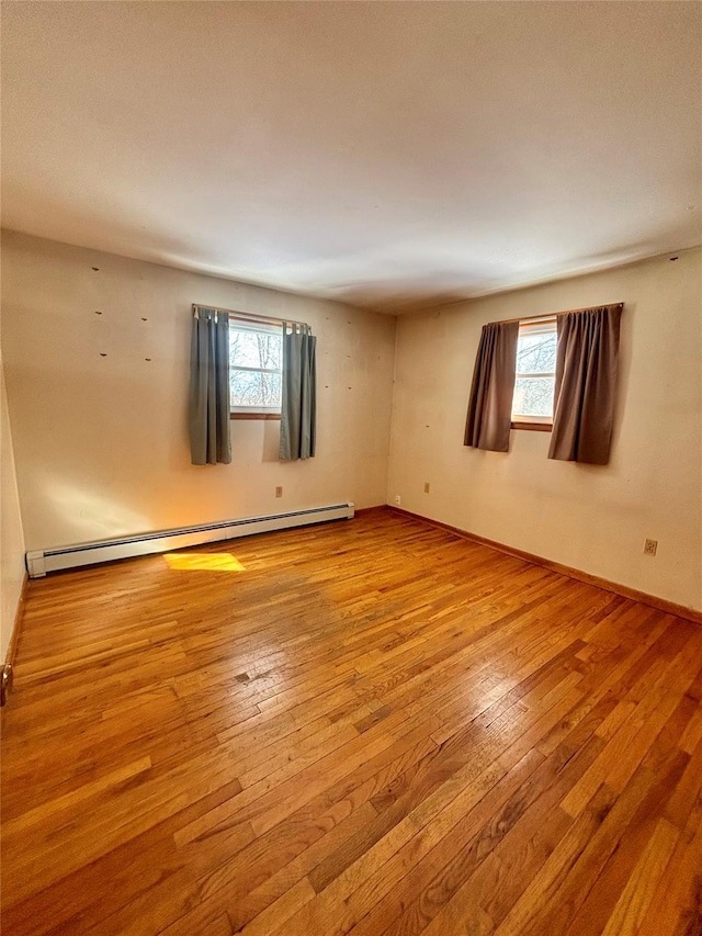 spare room featuring light wood-style floors, a baseboard radiator, and baseboards