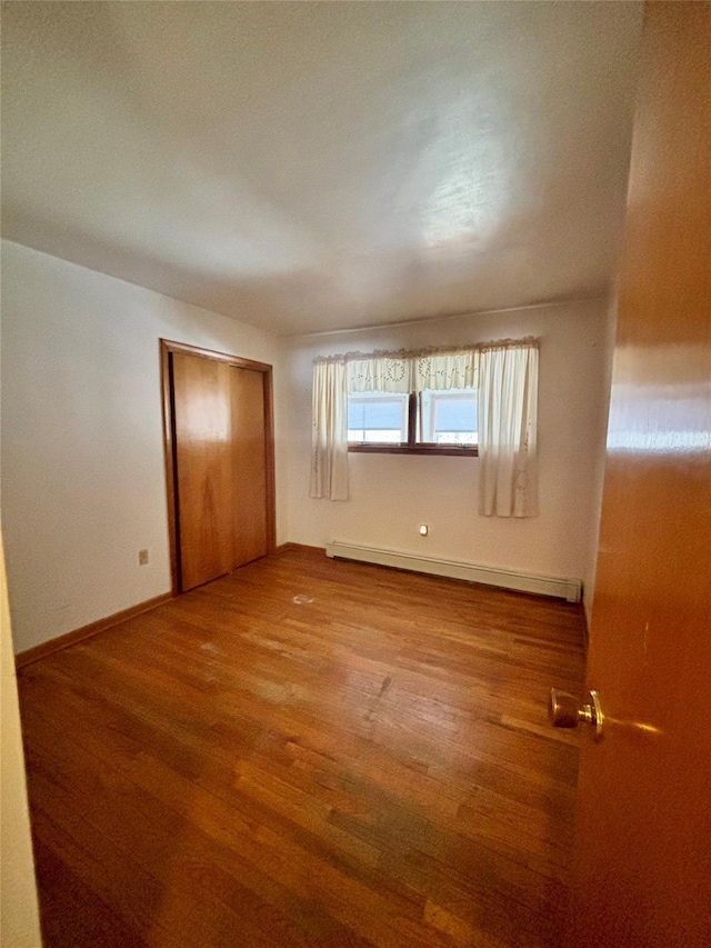 unfurnished bedroom with a baseboard heating unit, a closet, baseboards, and wood finished floors