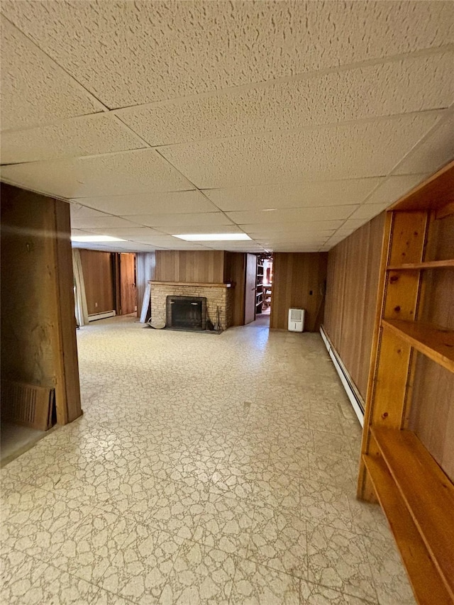 finished below grade area featuring a brick fireplace, a drop ceiling, wood walls, and baseboard heating