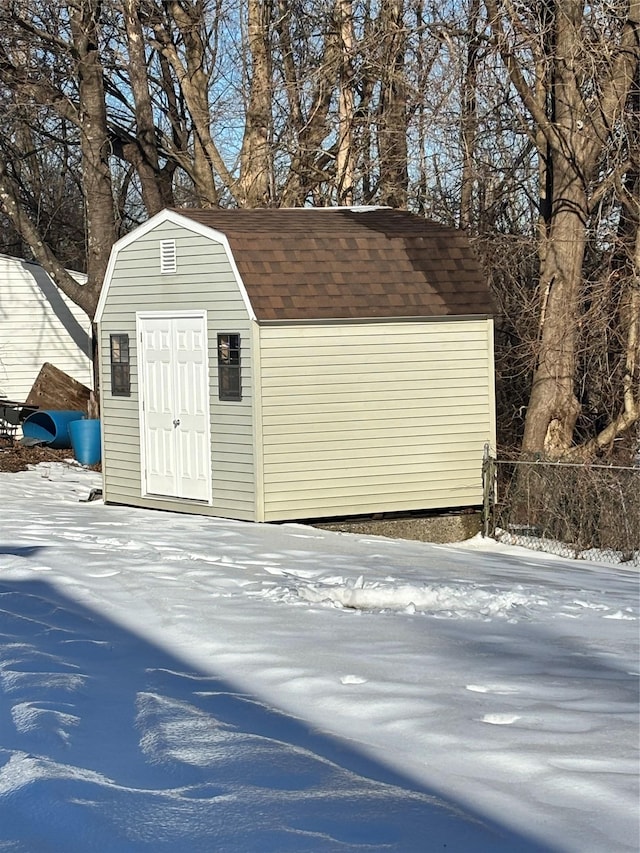 snow covered structure with a storage shed, fence, and an outbuilding