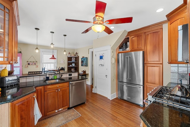 kitchen with sink, appliances with stainless steel finishes, hanging light fixtures, kitchen peninsula, and light wood-type flooring