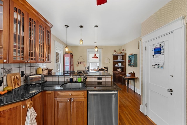 kitchen featuring sink, dark stone counters, hanging light fixtures, stainless steel dishwasher, and kitchen peninsula