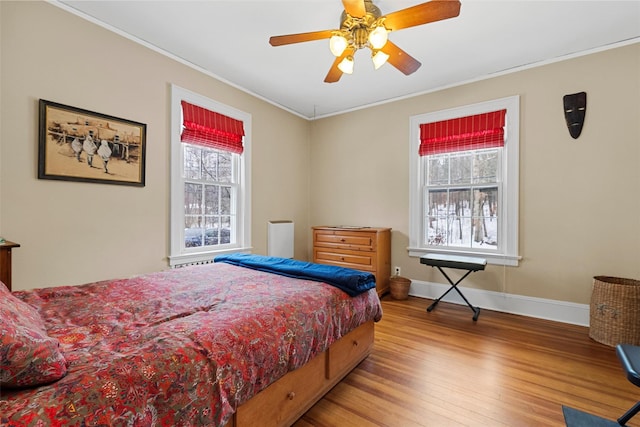 bedroom featuring multiple windows, hardwood / wood-style floors, ornamental molding, and ceiling fan