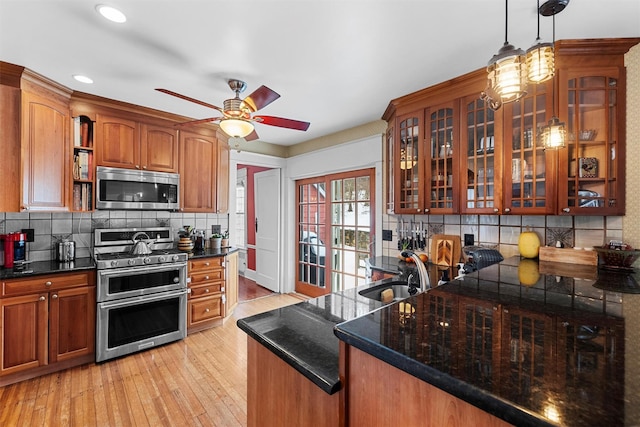 kitchen with appliances with stainless steel finishes, pendant lighting, sink, backsplash, and light hardwood / wood-style floors