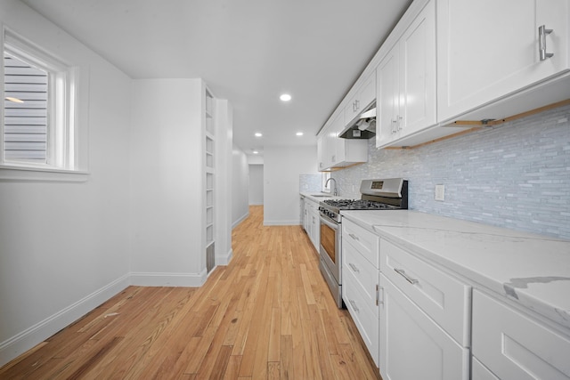 kitchen featuring stainless steel gas stove, white cabinetry, sink, backsplash, and light stone counters