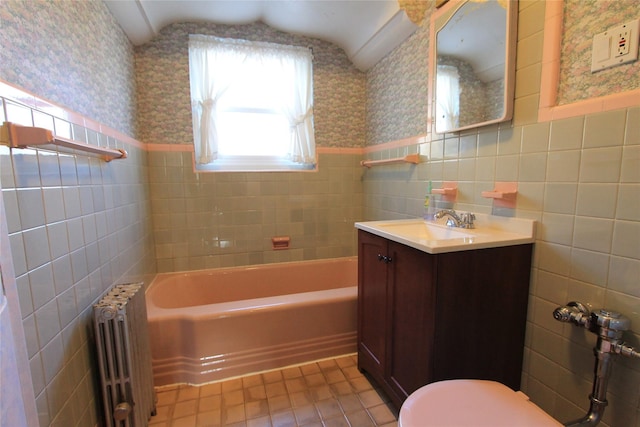 bathroom with radiator heating unit, tile walls, a tub to relax in, vanity, and toilet