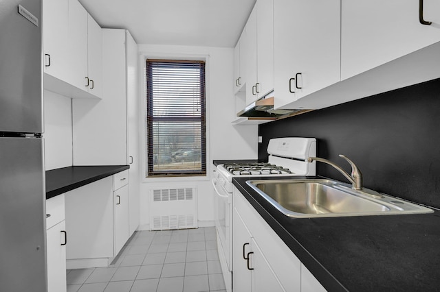 kitchen with white range with gas stovetop, a sink, white cabinets, freestanding refrigerator, and dark countertops