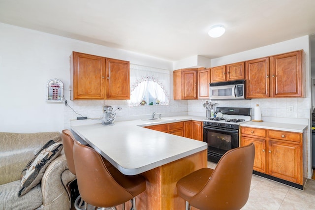 kitchen featuring gas range, decorative backsplash, kitchen peninsula, and a breakfast bar area