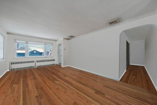 empty room featuring wood-type flooring and radiator heating unit