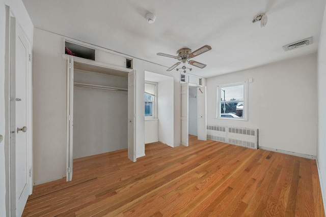 unfurnished bedroom featuring ceiling fan, two closets, radiator heating unit, and light wood-type flooring