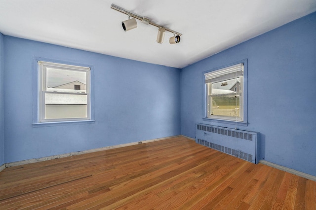 spare room featuring track lighting, radiator, and hardwood / wood-style floors