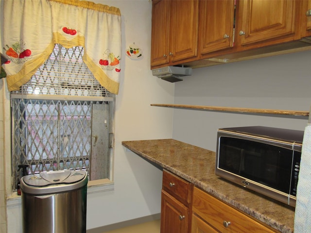 kitchen featuring black microwave, dark stone countertops, and brown cabinets